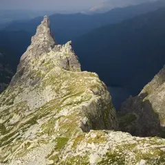Skalisty szczyt w Tatrach z widokiem na ciemną dolinę i jezioro.