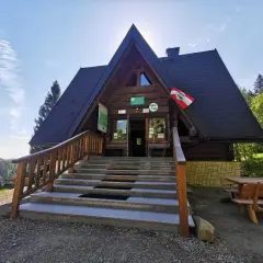 Drewniana bacówka pod honem, z kamiennymi schodami i drewnianą balustradą, zaprasza turystów. Flaga Polski powiewa na dachu.
