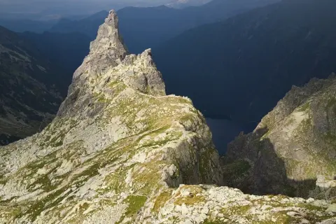 Skalisty szczyt w Tatrach z widokiem na ciemną dolinę i jezioro.