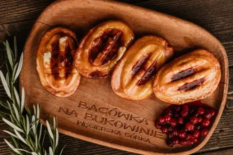Cztery grillowane oscypki z żurawiną i rozmarynem na drewnianej desce.