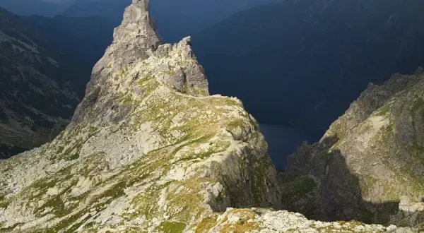 Skalisty szczyt w Tatrach z widokiem na ciemną dolinę i jezioro.
