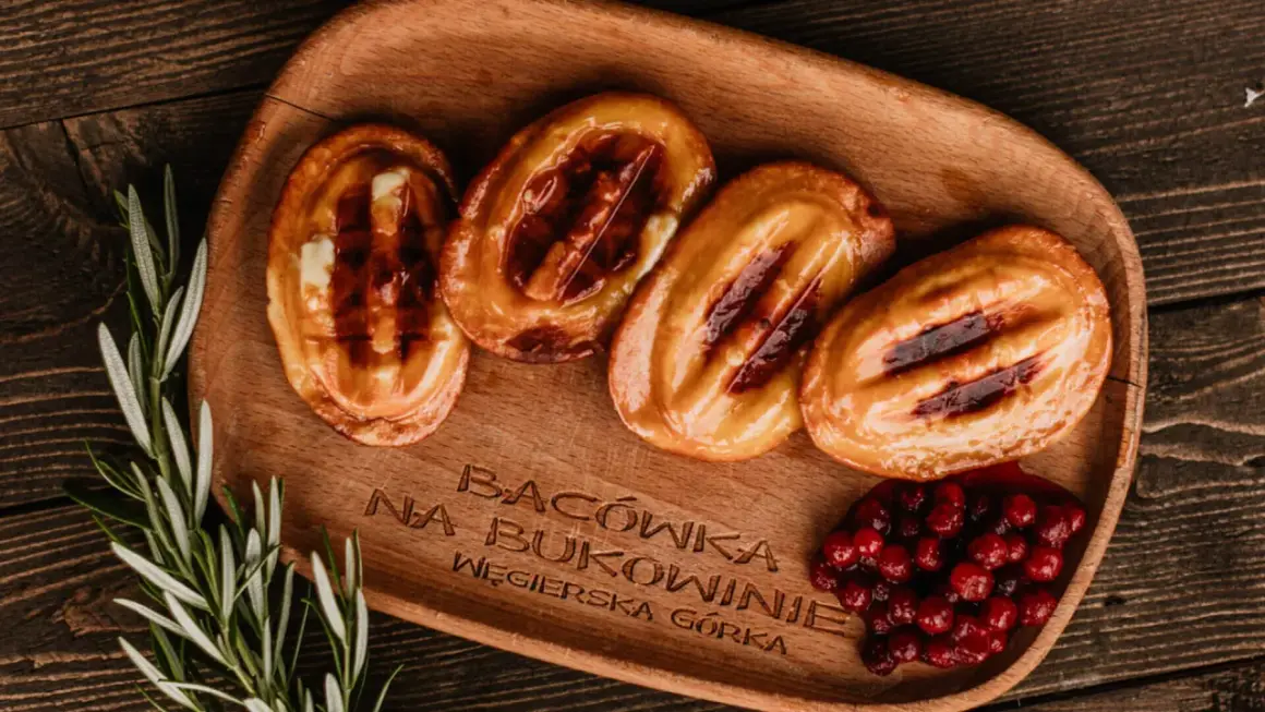 Cztery grillowane oscypki z żurawiną i rozmarynem na drewnianej desce.